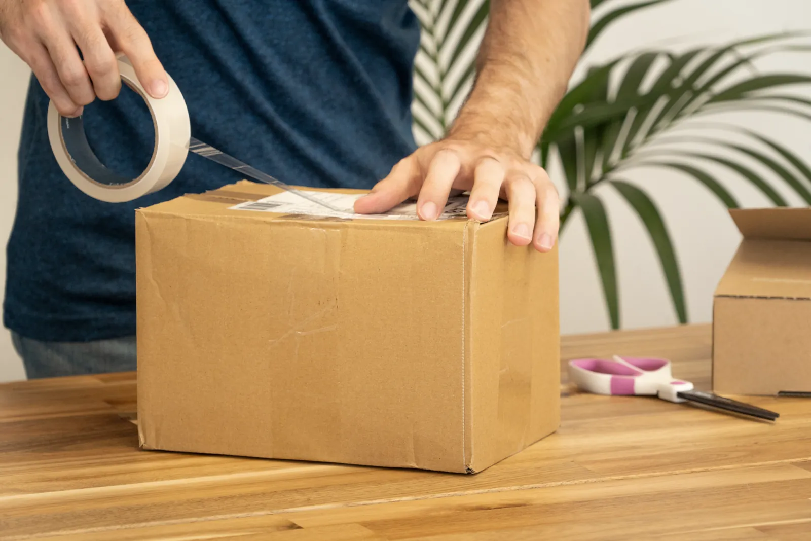 Manos cerrando con cinta una caja de cartón para enviar a Perú
